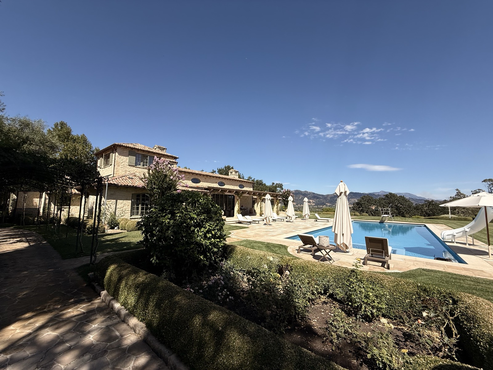 Pool area with house, mountains, and loungers